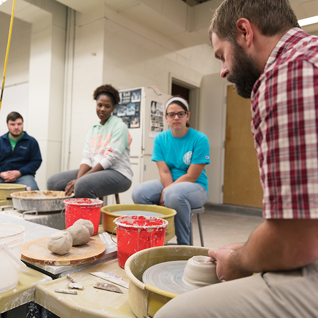 Professor at pottery wheel demonstrating proper technique to students.