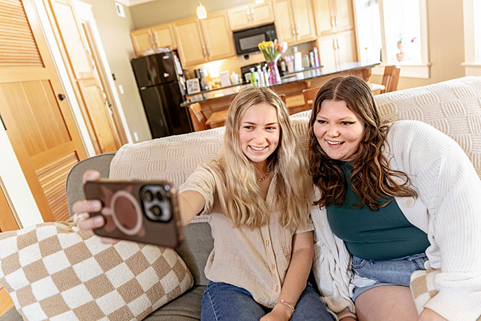 Two female students take a selfie while sitting on a sofa in a dorm room