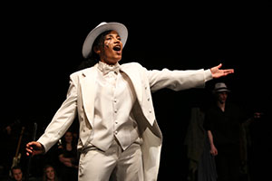 Striking photo of actress from the Musical Theater Showcase sings on stage while in a white suit and white hat