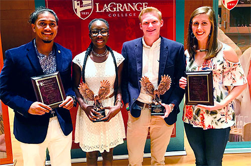 four students stand with their athletic awards following the reception