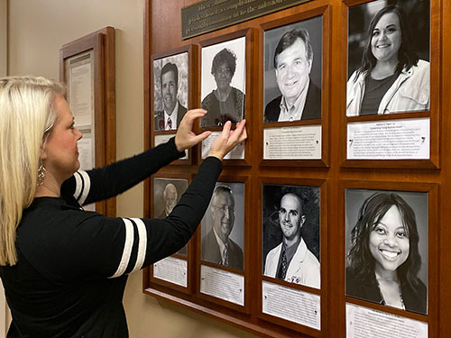 Leslie Sebaugh adjusts a photo on the Wall of Distinguished Alumni