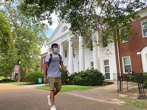 A student wearing a mask walks in front of Pitts Hall