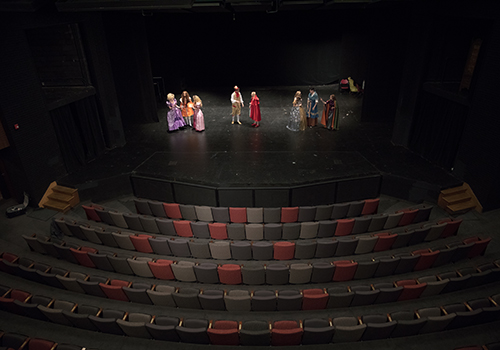Wide shot of Price Theater interior with stage and front rows of seating, while students rehearse on stage