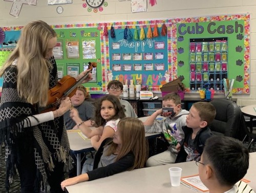 An LC student teacher shows students a violin.