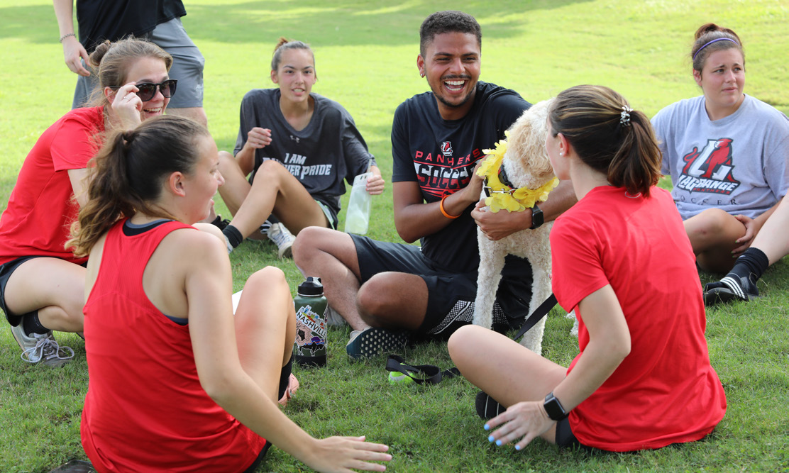 A group of students sits on the bright green grass laughing and smiling