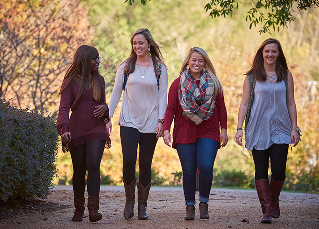 {Four female students walk towards the camera on an autumn day}
