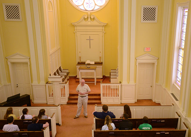 {Male professor addresses a small group of students int he college chapel}