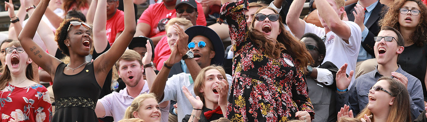 Many cheering faces in stadium seating. three rows and ten across.