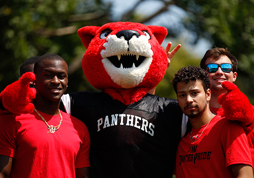 Three students pose with the college mascot, Pouncer