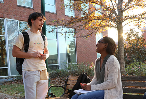 Two students chat outside on a sunny fall day