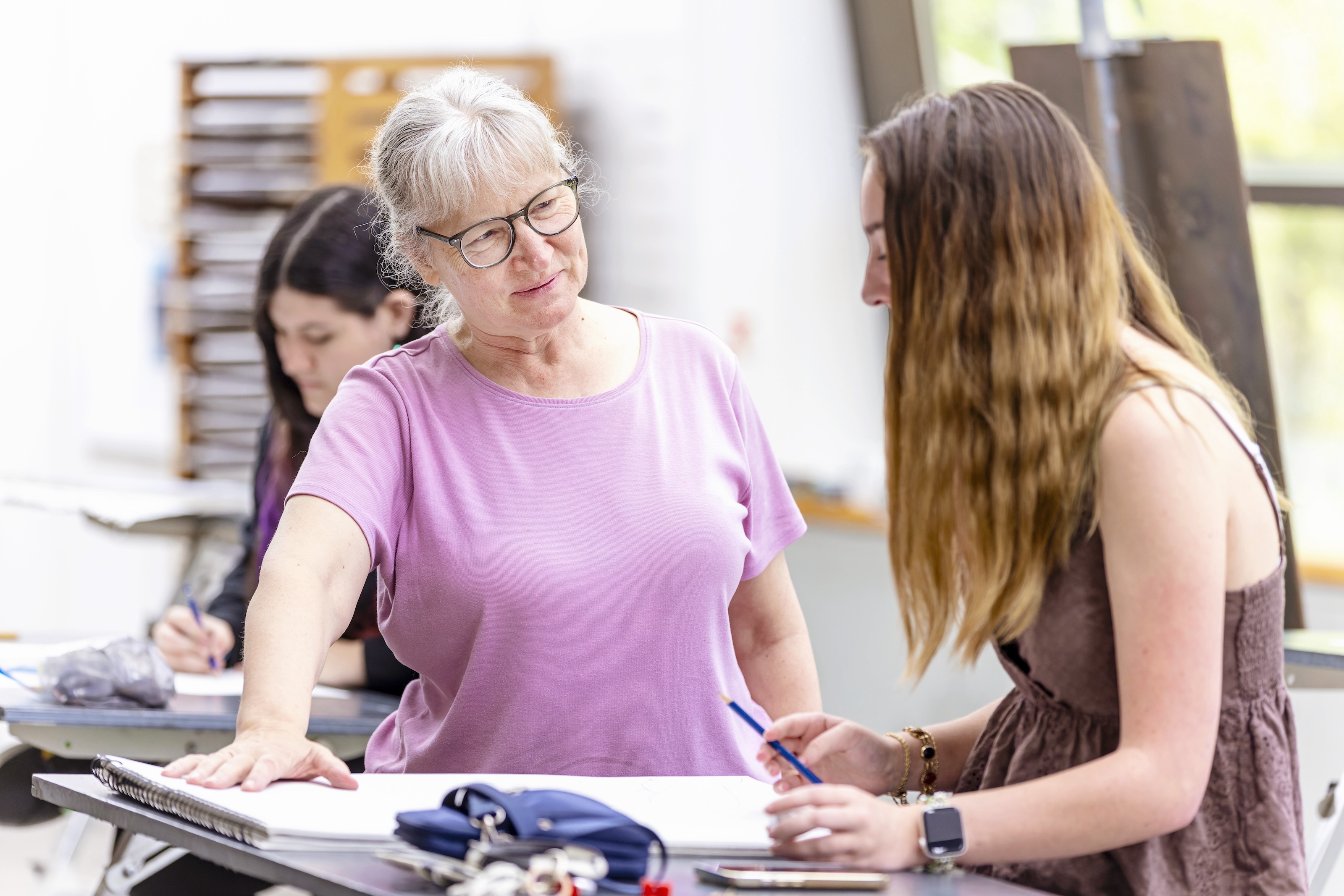A professor explains pottery techniques to a seated female student.