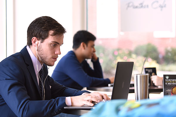 A man in a suit works on a laptop in a cafe