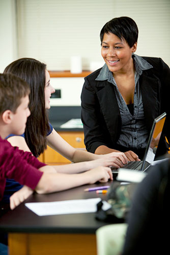 Female teacher speaking to high school aged children at a desk