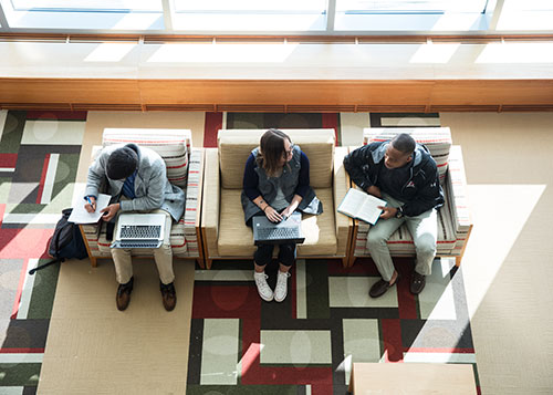 Three students sit in the library studying