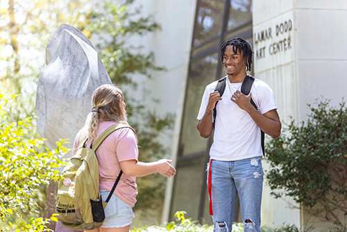 Two students stand outside Lamar Dodd Art Center on a bright, sunny day. 