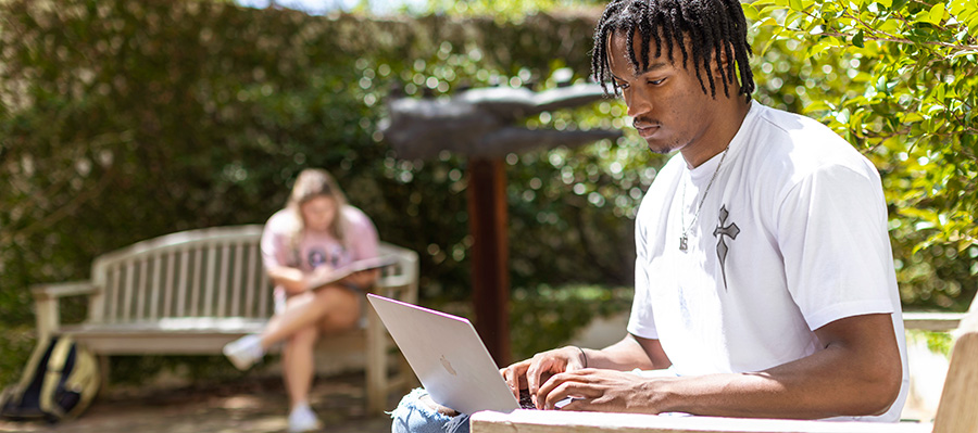 A male student works on a brightly lit bench and works on a laptop