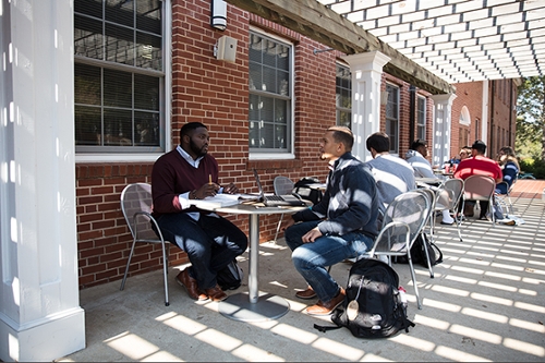 Two students sitting at a table and studying underneath the pergola on the porch of Turner Hall