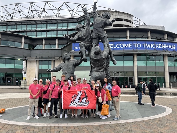 Students, faculty, and staff on Study Away trip standing with college flag in front of Twickenham Stadium