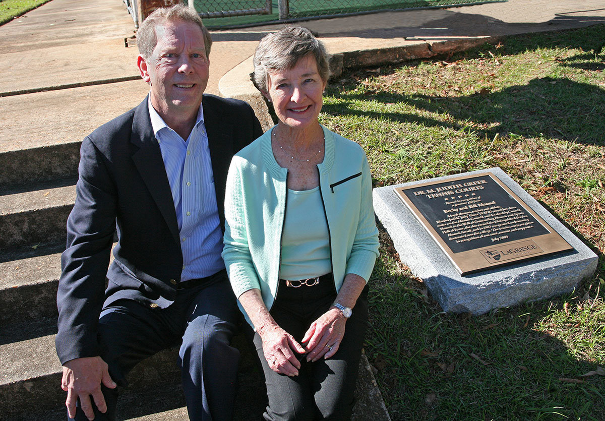 Bill and Becky Manuel sit on a hill next to their dedication plaque.