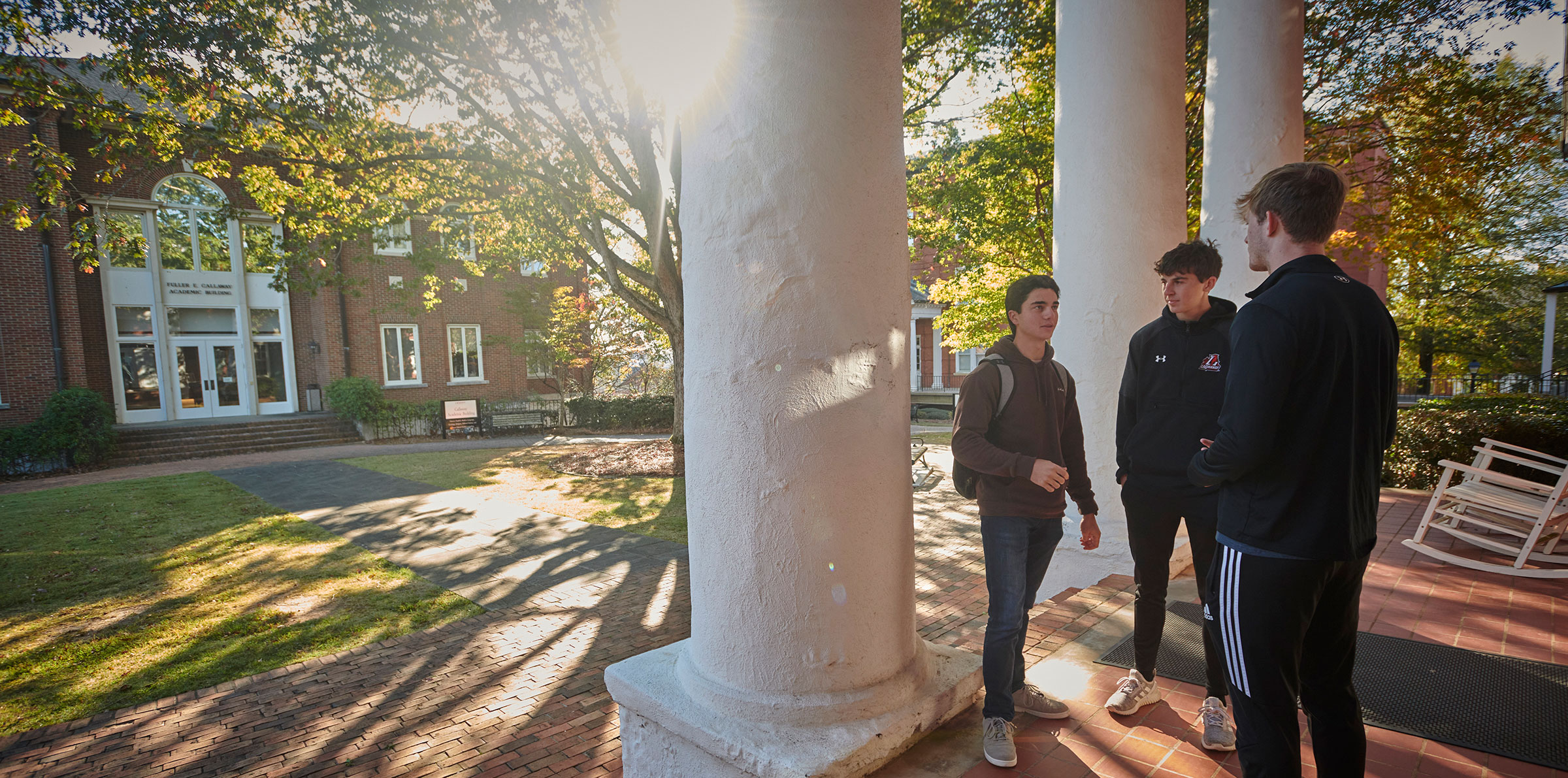 Three male college students standing in front of Smith Hall